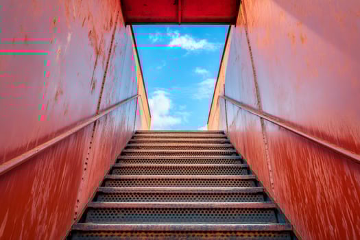 Rusty metal staircase leading to a blue sky with clouds photo