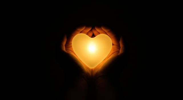 A pair of hands gently holding a glowing heart shaped light in a dark environment, symbolizing warmth and love radiating from within. photo