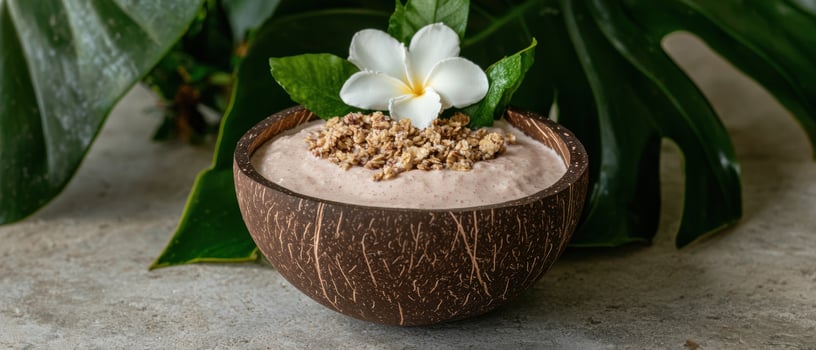 A smoothie bowl in a coconut shell with granola and a flower photo