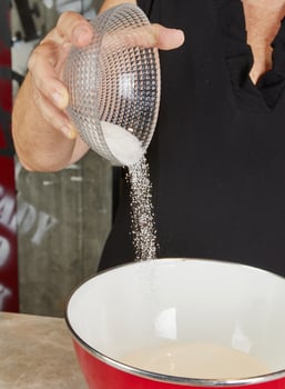 Sugar being poured from a clear bowl into a mixing bowl, preparing ingredients for a dessert in the kitchen photo