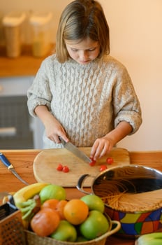 The girl carefully cuts the tomatoes, trying to make even pieces, while her mom smiles, watching her. photo