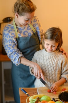 Mom slices cucumbers while the daughter adds bright red tomato pieces to the bowl. photo