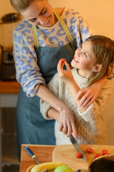 The girl laughs as she accidentally drops a piece of tomato, and her mom picks it up with a smile. photo