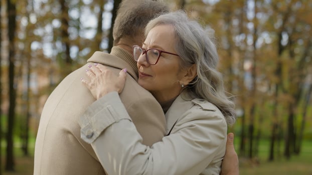 Happy mature senior middle aged Caucasian woman female hugging embracing man male affectionate bonding old couple in love grandparents hug embrace cuddle support care tender cuddling meeting outdoors photo