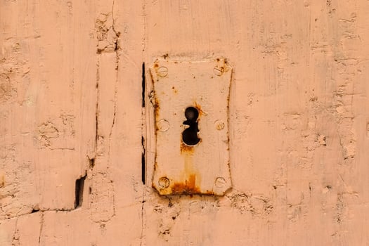 Rusty keyhole on a decaying peach-colored wooden door photo