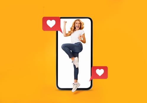 A young woman joyfully expresses excitement while interacting with a smartphone. The bright background and heart icons symbolize love and modern communication in dating. photo