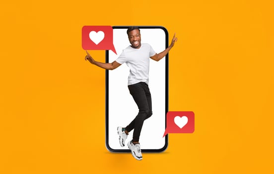 A young man is playfully engaging with a smartphone, showcasing love and connection through social media messages. The background is bright orange, creating a vibrant atmosphere. photo