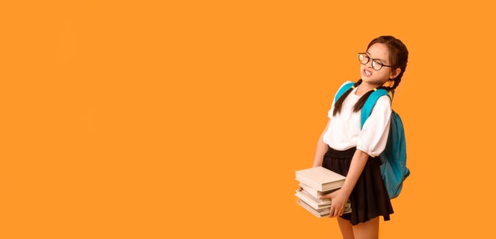 Too Much Homework. Discontented Asian School Girl Carrying Heavy Books Over Yellow Studio Background. Copy Space photo