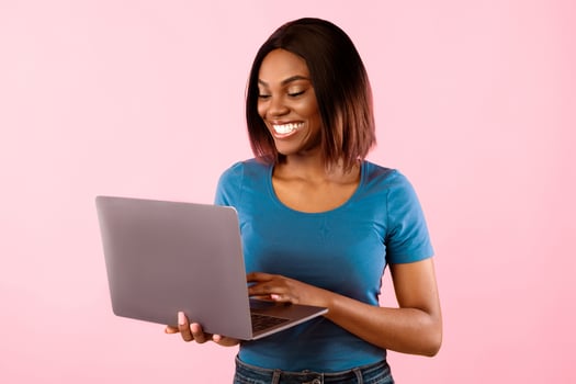 Happy black woman using laptop computer browsing internet posing standing over yellow studio background. People and gadgets, technologies, great website for freelancers concept photo
