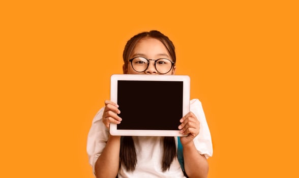 Online Class. Japanese Schoolgirl Showing Digital Tablet Blank Screen Recommending Educational Application Standing Over Yellow Studio Background photo