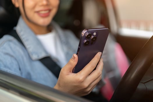 A close-up of a positive Asian woman using her smartphone while stopped at traffic in the city. photo