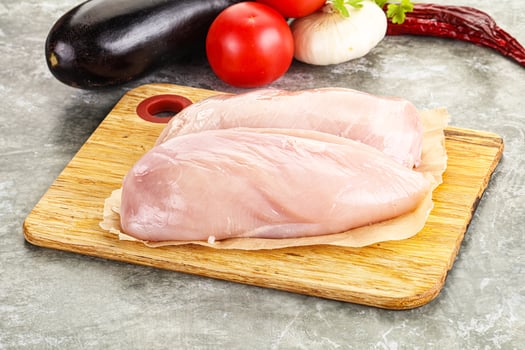 Two raw chicken breasts on a cutting board with vegetables photo