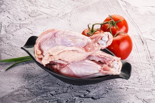 Raw chicken legs in a black bowl with tomatoes photo