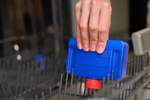 Hand placing dishwasher cleaner bottle in empty dishwasher photo