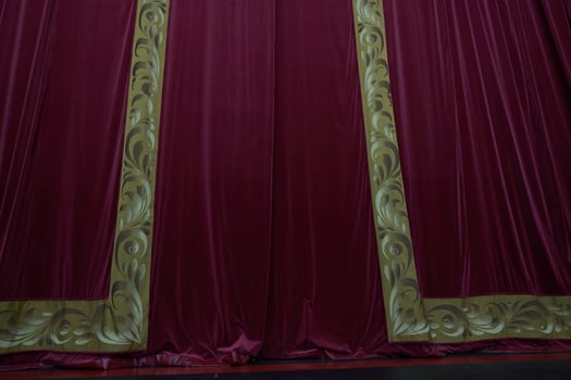 A red curtain with vertical pleats, illuminated in a theatrical setting, showcasing the rich dense texture of the fabric with room to copy photo