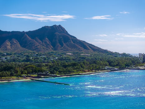 Aerial view of Diamond Head Crater on Oahu island, with turquoise waters, sandy beach, seawall, lush greenery, and scattered buildings in Honolulu. photo