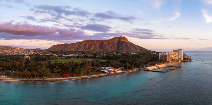 Aerial view of Diamond Head Crater on Oahu Island, Hawaii, at sunset. Turquoise waters, palm lined shore, and high rise buildings are visible. photo