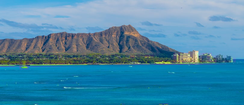 Diamond Head Crater on Oahu island with rugged ridges, Pacific Ocean, small boats, surfers, Honolulu skyline, sandy beaches, and lush greenery. photo