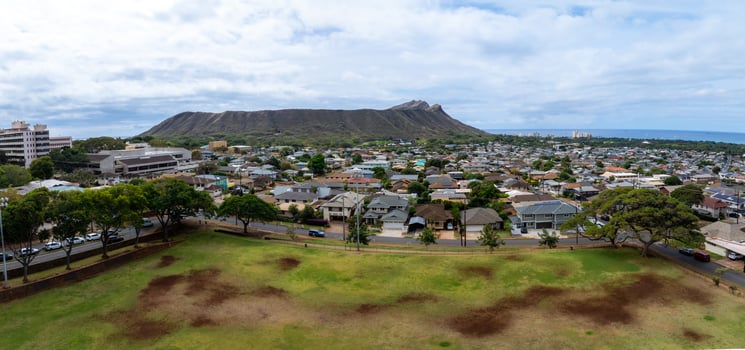 Panoramic aerial view of a residential area in Oahu, Hawaii, featuring Diamond Head Crater, a grassy park, houses, and the ocean on the horizon. photo