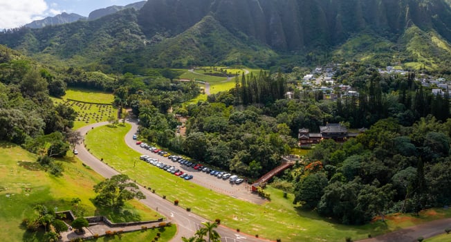 Aerial view of Byodo In Temple in Oahu, Hawaii, with a red bridge, lush greenery, Ko olau Mountain Range, winding roads, and nearby cemetery. photo