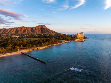 Aerial view of Waikiki Beach in Honolulu, Hawaii, with Diamond Head Crater in the background, turquoise waters, a pier, and beachfront hotels at sunset. photo