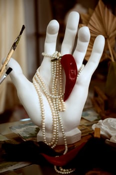 plaster hand holding pearl necklace and red hot pepper. close-up hand made of white plaster, paint brushes nearby. concept hot classic photo