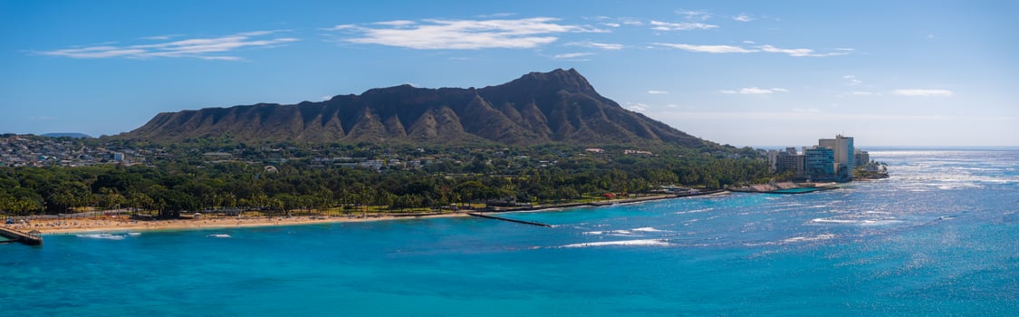 Aerial view of Diamond Head Crater on Oahu island, with turquoise waters, sandy Waikiki Beach, urban buildings, and a clear blue sky with clouds. photo