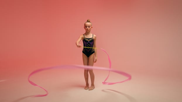 Caucasian little girl kid daughter schoolgirl female gymnast schoolgirl child dancer ballerina athlete perform gymnastics exercise twirling spinning gymnastic tape dance ballet studio pink background photo