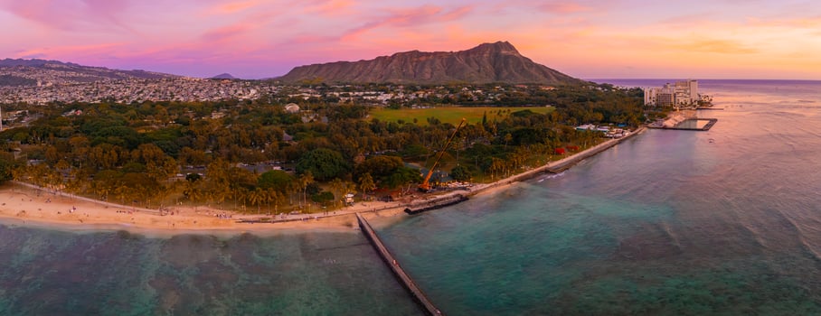 Aerial view of Waikiki Beach in Honolulu, Hawaii, with Diamond Head Crater in the background, sandy shores, turquoise waters, and urban structures at sunset. photo