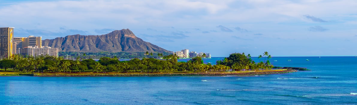 View of Diamond Head Crater on Oahu island, with lush greenery, Honolulu's high rise buildings, and calm Pacific waters under a partly cloudy sky. photo