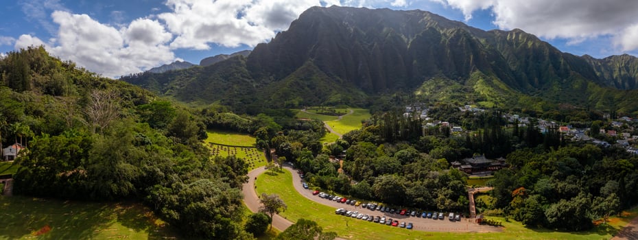 Aerial view of the Byodo In Temple surrounded by lush greenery, with the Ko olau mountain range in the background and a park in the foreground. photo