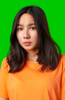 Young woman with long dark hair in orange shirt expresses curiosity against a bright green background photo