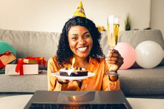 Online Birthday Party. Happy African American Woman At Laptop Celebrating B-Day Holding Cake With Candle And Wearing Festive Hat Sitting At Home, Smiling To Camera. Holiday, Distant Celebration photo
