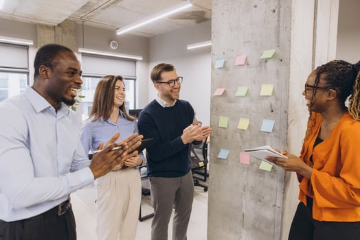 Professional team applauding female executive following compelling presentation near whiteboard wall in contemporary workspace photo