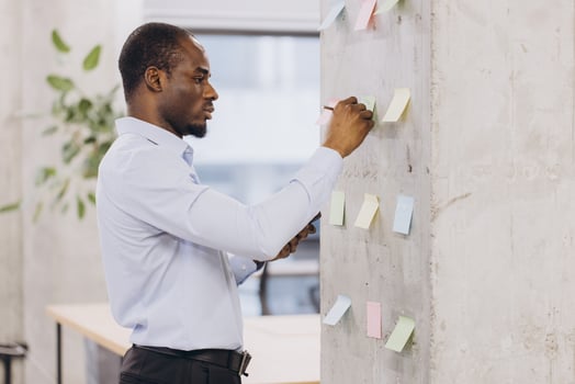 African american business professional organizing ideas on a wall with colorful sticky notes in a modern office setting, focusing on strategic planning and collaboration photo
