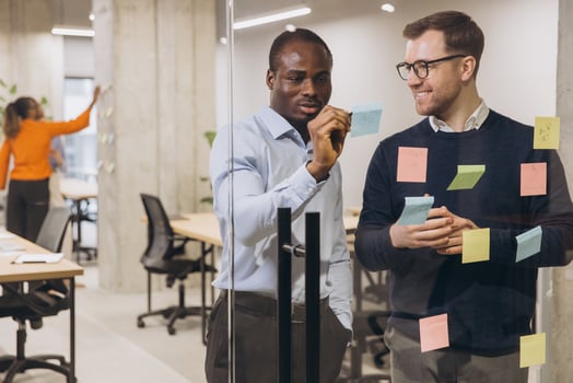 Two professional men discussing ideas with sticky notes on a glass wall in a contemporary office, promoting teamwork and innovation photo