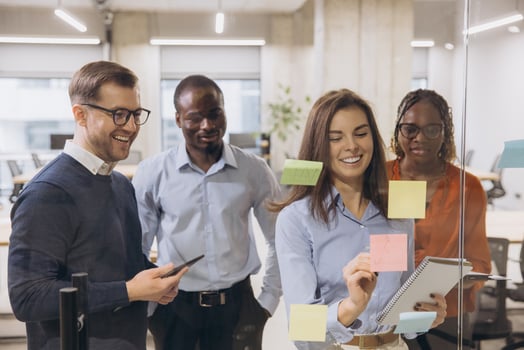 Business professionals collaborating, placing colorful sticky notes on glass wall during innovative team brainstorming meeting photo