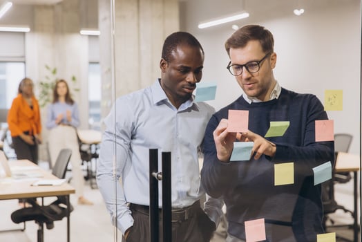 Diverse business team brainstorming, collaborating near glass wall with colorful sticky notes, showcasing innovative workplace interaction photo