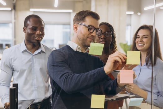 Diverse group of professionals engaging in a collaborative brainstorming session, using sticky notes on a glass wall in a modern office environment photo