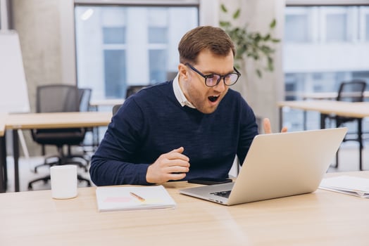 Surprised businessman looking at laptop in office with shocked facial expression, receiving unbelievable news photo