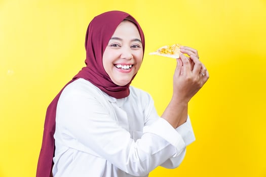 a beautiful asian woman in a hijab eating pizza on yellow background photo
