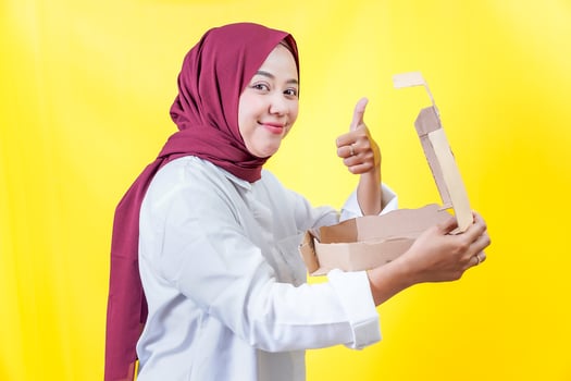a woman in a hijab holding a box with a thumbs up photo