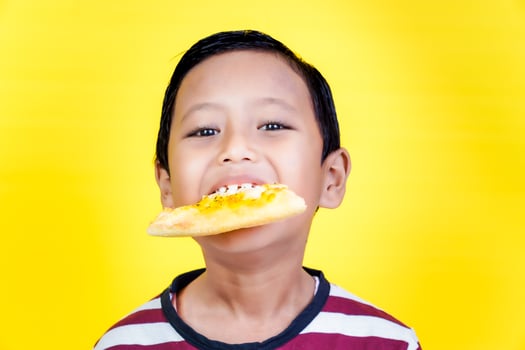 Close up of cheerful boy bites a slice of pizza in his mouth photo