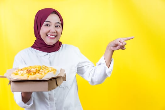 A cheerful asian woman in a hijab happily presents a delicious pizza photo