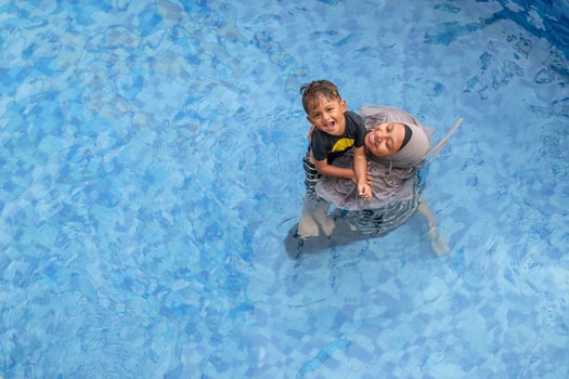 Beautiful Asian mother playing with son in swimming pool, view from above. Asian middle-aged mother and seven years old daughter. Happy moment together. photo