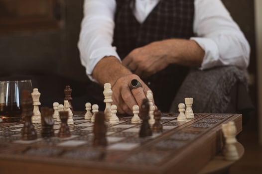 ingers resting on a knight, his signet ring reflects the tension of the match in the dim light. photo