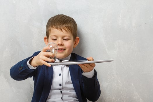 Cute little schoolboy with light bulb on grey background photo