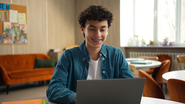 Smiling Caucasian man male teenage happy guy student schoolboy pupil modern technology service study exam using laptop computer e-learning learn studying online internet education in school university photo