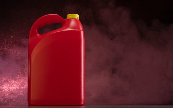 Front view of red plastic motor oil bottle, container with handle and yellow screw cap without label against dark background photo