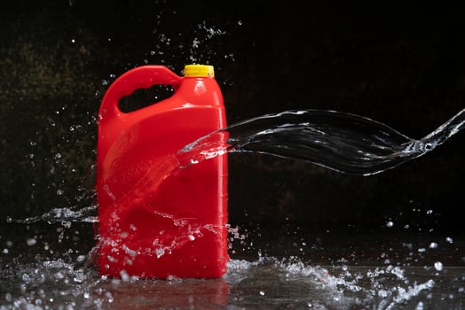 Front view of red plastic motor oil bottle splashed by stream of water, container with handle and yellow screw cap without label photo